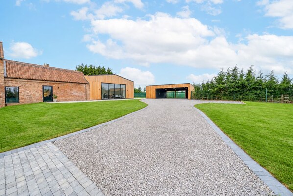 A building with a gravel driveway leading to a modern entrance, surrounded by well-maintained grass and trees.