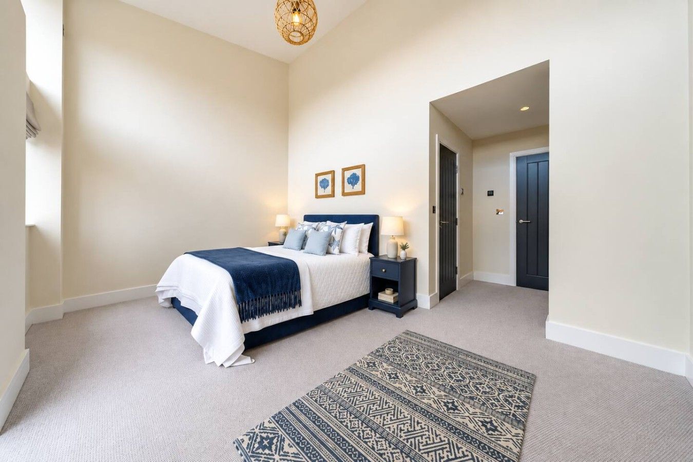 A bedroom with a bed, bedside tables, a rug, and a door leading to another room.