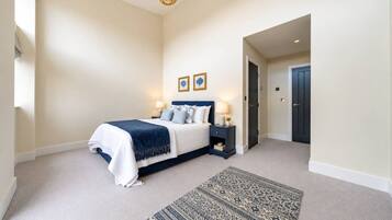 A bedroom with a bed, bedside tables, a rug, and a door leading to another room.