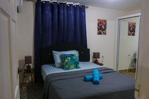 Ein Hotelzimmer mit einem Bett, einem blauen Vorhang, einem Nachttisch mit einer Lampe und zwei Bildern an der Wand.
