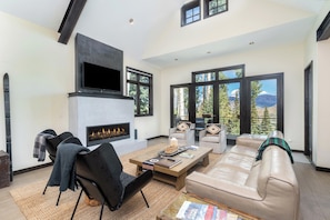 A modern living room with a fireplace, leather sofa, and large windows offering a mountain view. - Canyon View Escape 6 bedrooms sleeps 16 (Telluride)