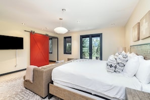 A bedroom with a large bed, a red barn-style door, a flat-screen TV, and a view of trees through the windows. - Canyon View Escape 6 bedrooms sleeps 16 (Telluride)