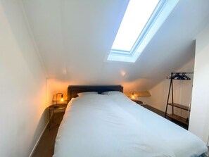 Ein Schlafzimmer mit Oberlicht, einem Bett, Nachttischlampen und einer Kleiderstange.