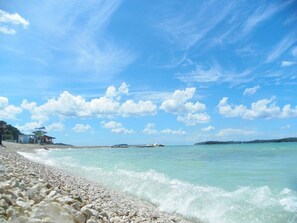 Ein Strand mit Kieselsteinen, ruhigem Wasser und blauem Himmel.