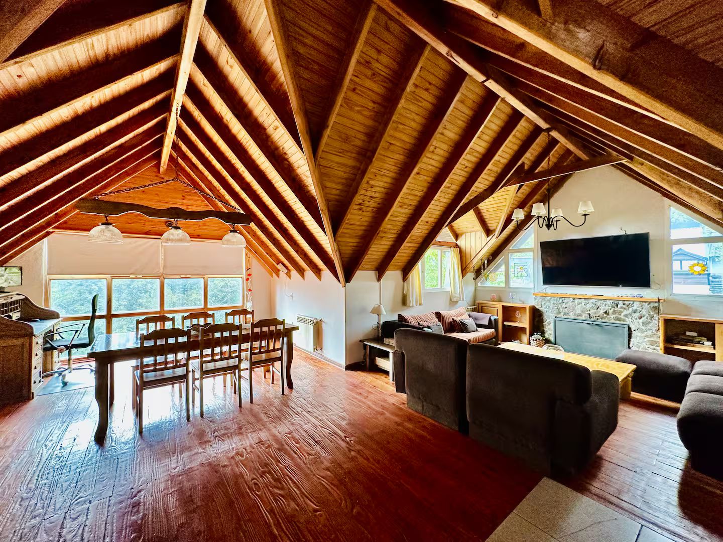 Un dormitorio en el ático con techo de madera alto, una zona de comedor con sillas y mesa, un sofá, un televisor y una chimenea de piedra.