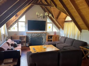 Ein gemütliches Wohnzimmer im Loft-Stil mit Kamin aus Stein, einem Flachbildfernseher und einem großen Fenster.