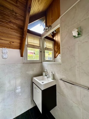 Een badkamer met een wit wastafelmeubel, een spiegel en een raam met houten luiken.