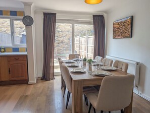 Ein Essbereich mit einem Holztisch, gedeckt für vier Personen, einer Uhr an der Wand und Blick auf ein Backsteingebäude.