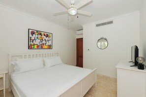 Quarto com cama, ventoinha no teto, ar condicionado fixado na parede, porta e espelho.