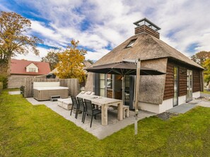 Ein Reetdachhaus mit Terrasse, Whirlpool und Essbereich.