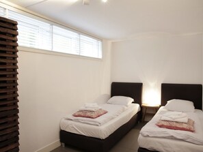 Ein Hotelzimmer mit zwei Betten, weißer Bettwäsche und einem Fenster mit Jalousien.
