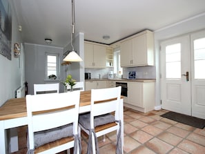 A modern kitchen with white cabinetry, a dining table with chairs, and a pendant light. - Michels Hues Holiday Apartment 1 (Sylt)