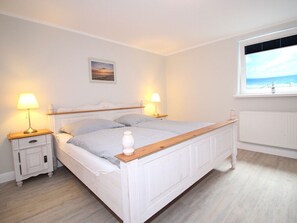 A bedroom with a bed, two bedside tables, a nightstand, a window with a view, and a wall-mounted picture. - Michels Hues Holiday Apartment 1 (Sylt)
