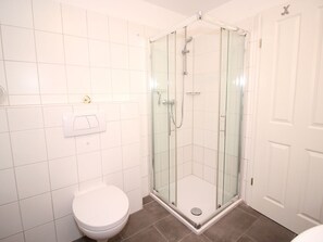 A bathroom with a glass-enclosed shower, a white toilet, and a white door. - Michels Hues Holiday Apartment 1 (Sylt)