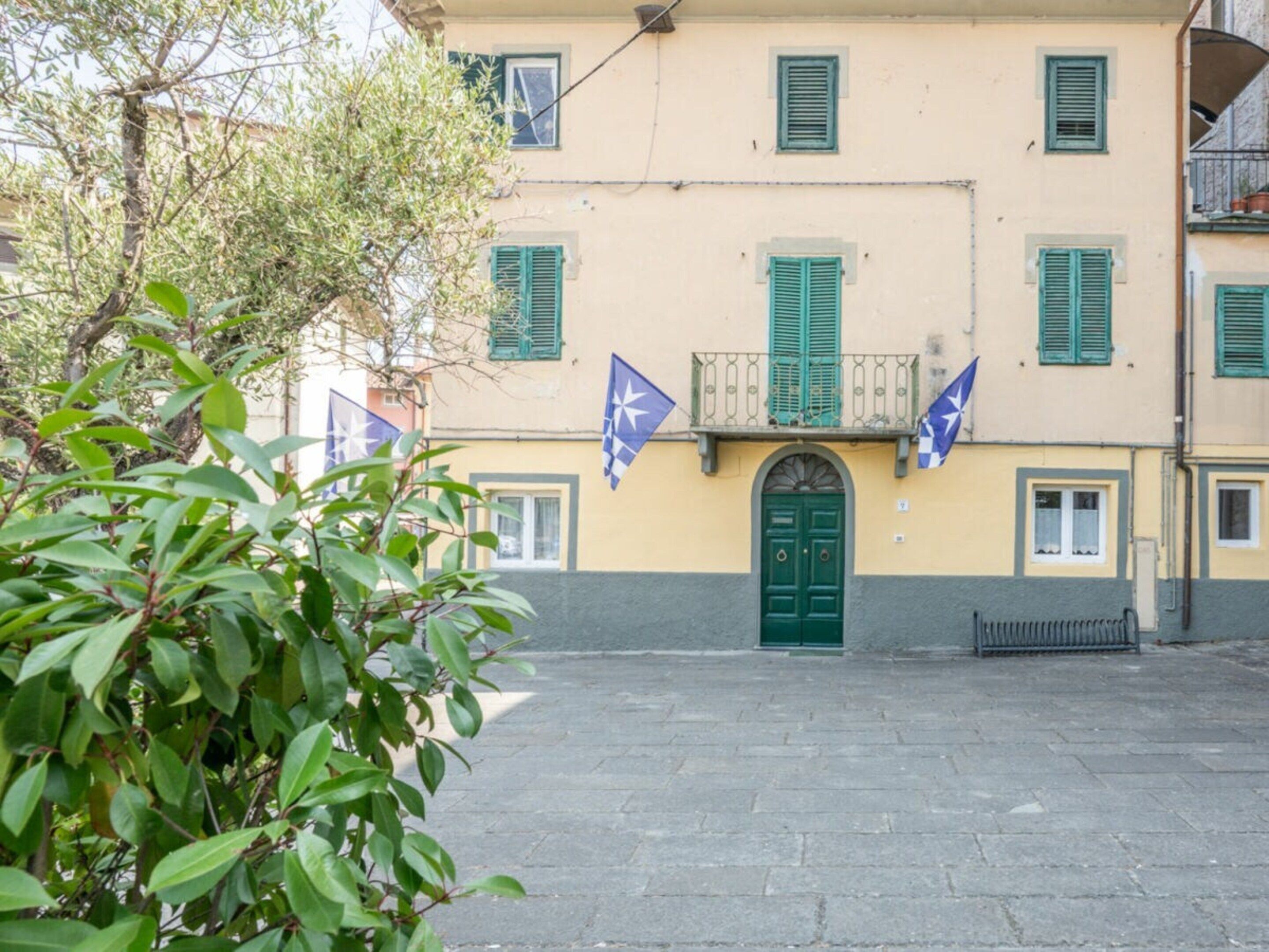 Un edificio con una porta verde, diverse finestre con persiane e due bandiere.