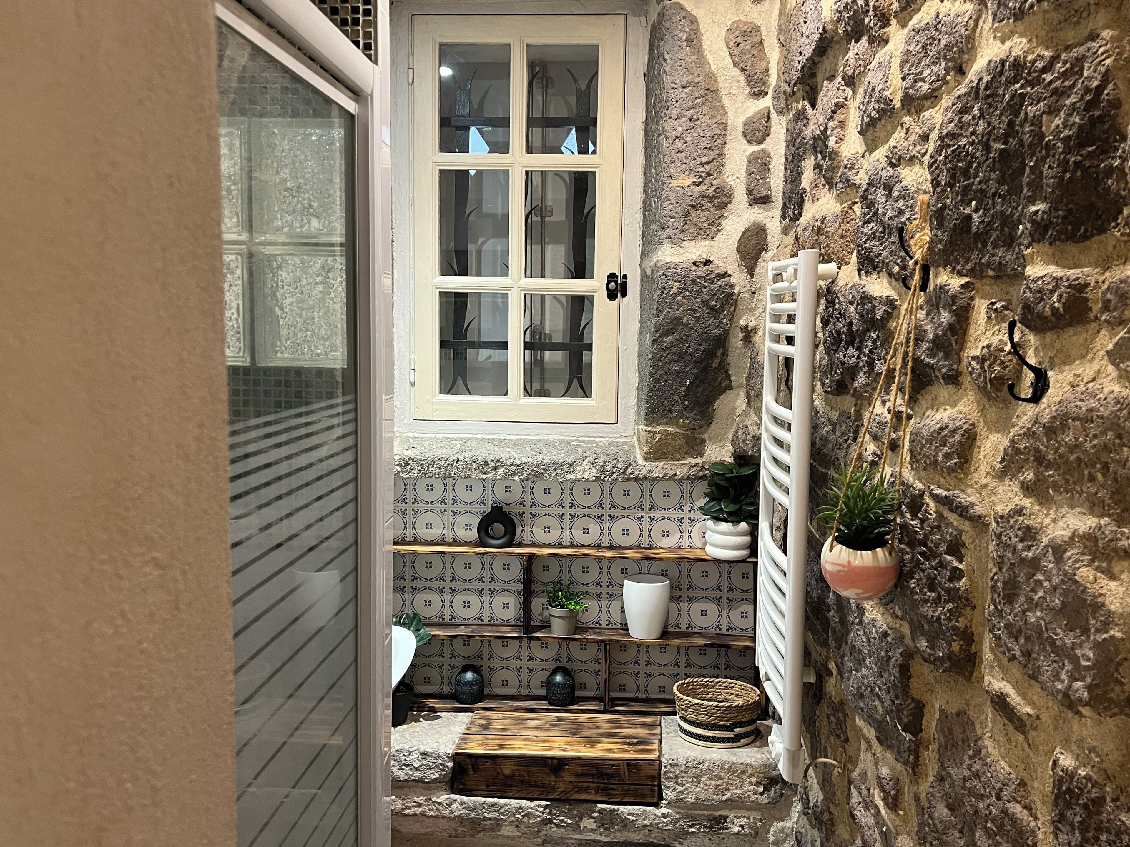 Une salle de bain aux murs en pierre, dotée d’une fenêtre, d’étagères pour les articles de toilette et d’un porte-serviettes.