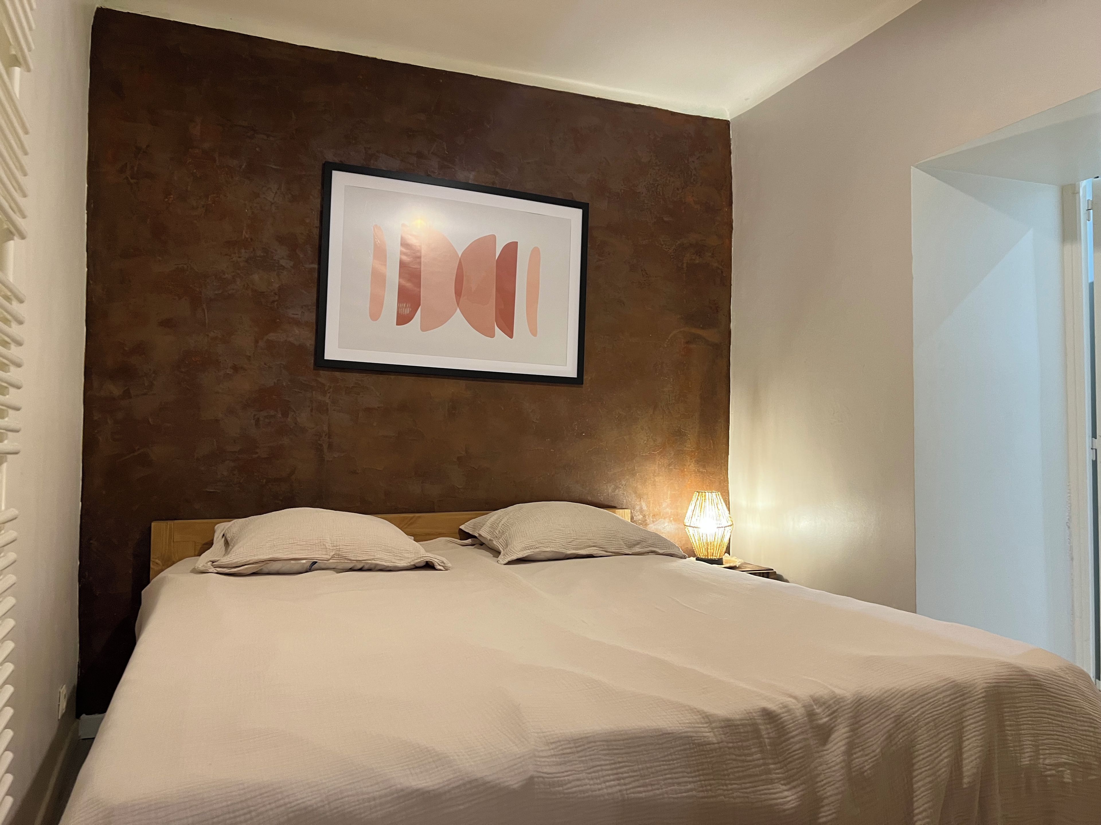 Una camera d'albergo con un letto, un quadro appeso al muro e una lampada da comodino.