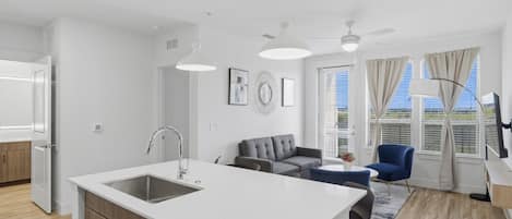 Et moderne køkken med en central ø, et spiseområde med bord og stole, en sofa og en ventilator i loftet.