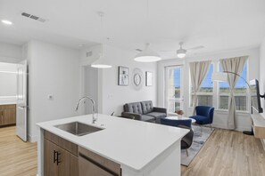 A modern kitchen with a central island, a dining area with a table and chairs, a sofa, and a ceiling fan. - Beautiful 2BR near PGA and Universal Studios | Sleeps 6 (Frisco)