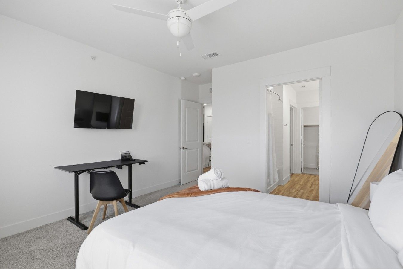 A hotel room with a bed, a desk, a chair, a television, and a door leading to another room.