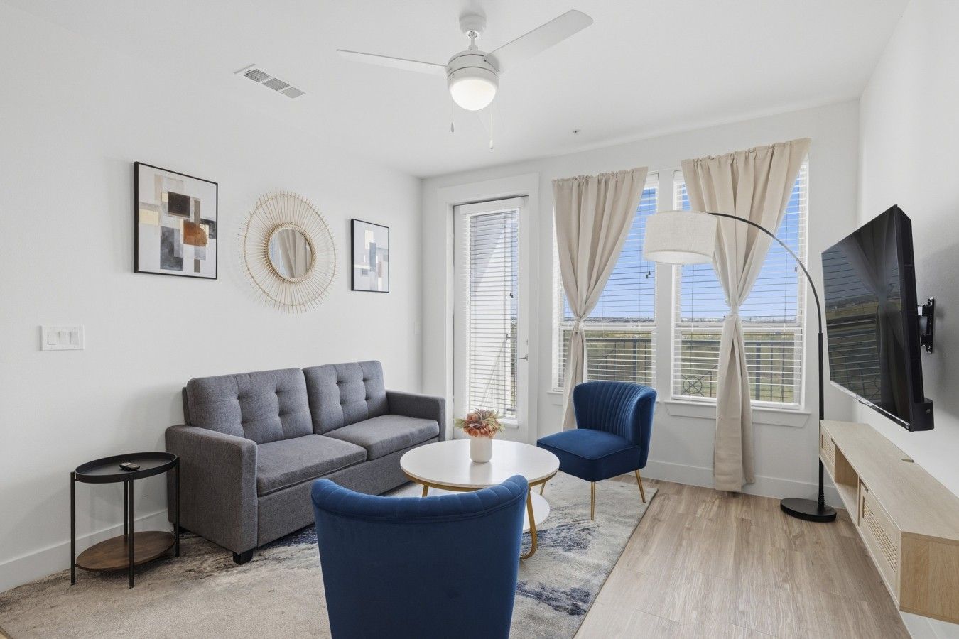 A modern living room with a grey sofa, blue armchairs, a round coffee table, and a flat-screen TV.