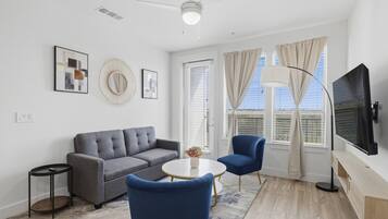 A modern living room with a grey sofa, blue armchairs, a round coffee table, and a flat-screen TV.