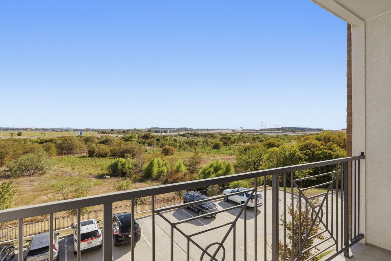 A balcony with a view of a parking lot and distant buildings.