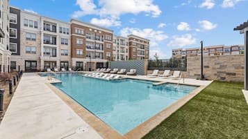 A swimming pool with lounge chairs and a building with multiple balconies in the background.