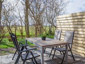 Eine Terrasse im Freien mit Tisch und Stühlen, umgeben von einem Holzzaun und Bäumen.