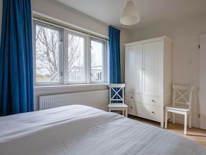 Ein Schlafzimmer mit Bett, einem Fenster mit Vorhängen, einem Kleiderschrank und einem Sessel.