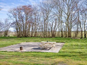 Ein Picknickbereich mit Tisch und Bänken, umgeben von einer Wiese und Bäumen.