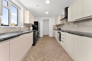 Une cuisine moderne avec un parquet en bois disposé en chevrons, des appareils en acier inoxydable et des meubles de cuisine blancs.