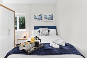 A hotel room with a bed, a bedside table with a coffee pot, a tray with breakfast items, and two abstract paintings on the wall. - 10 mins from city centre. 6 Bed all ensuite, contractor friendly whole house (Peterborough)