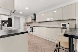 A modern kitchen with white cabinets, a black countertop, and a herringbone-patterned floor. - 10 mins from city centre. 6 Bed all ensuite, contractor friendly whole house (Peterborough)