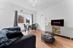 Uma sala de estar moderna com sofá, mesa de centro de vidro, televisão de tela plana e área de jantar com mesa e cadeiras.