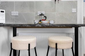 Cozinha com cafeteira, dois banquinhos e painel de azulejos.