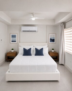Un dormitorio moderno con una cama grande, un ventilador de techo, equipo de aire acondicionado, mesitas de noche con plantas y obras de arte en las paredes.