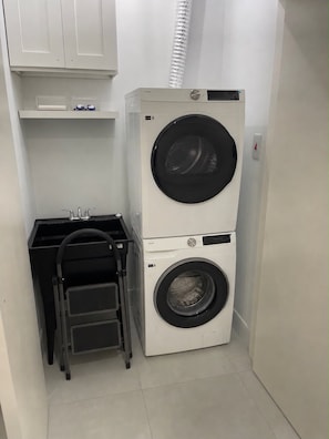 Un lavadero pequeño y funcional con lavadora y secadora apiladas, un lavamanos y una silla plegable.