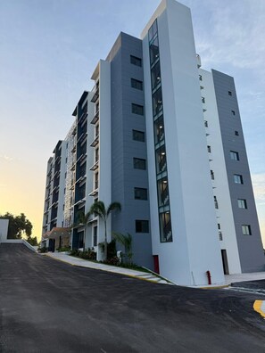 Un edificio residencial de varios pisos con un diseño arquitectónico moderno, que cuenta con balcones y un techo plano.