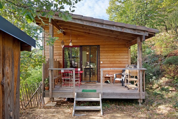 A wooden cabin with a covered porch, outdoor seating, and a glass door leading to an interior dining area.