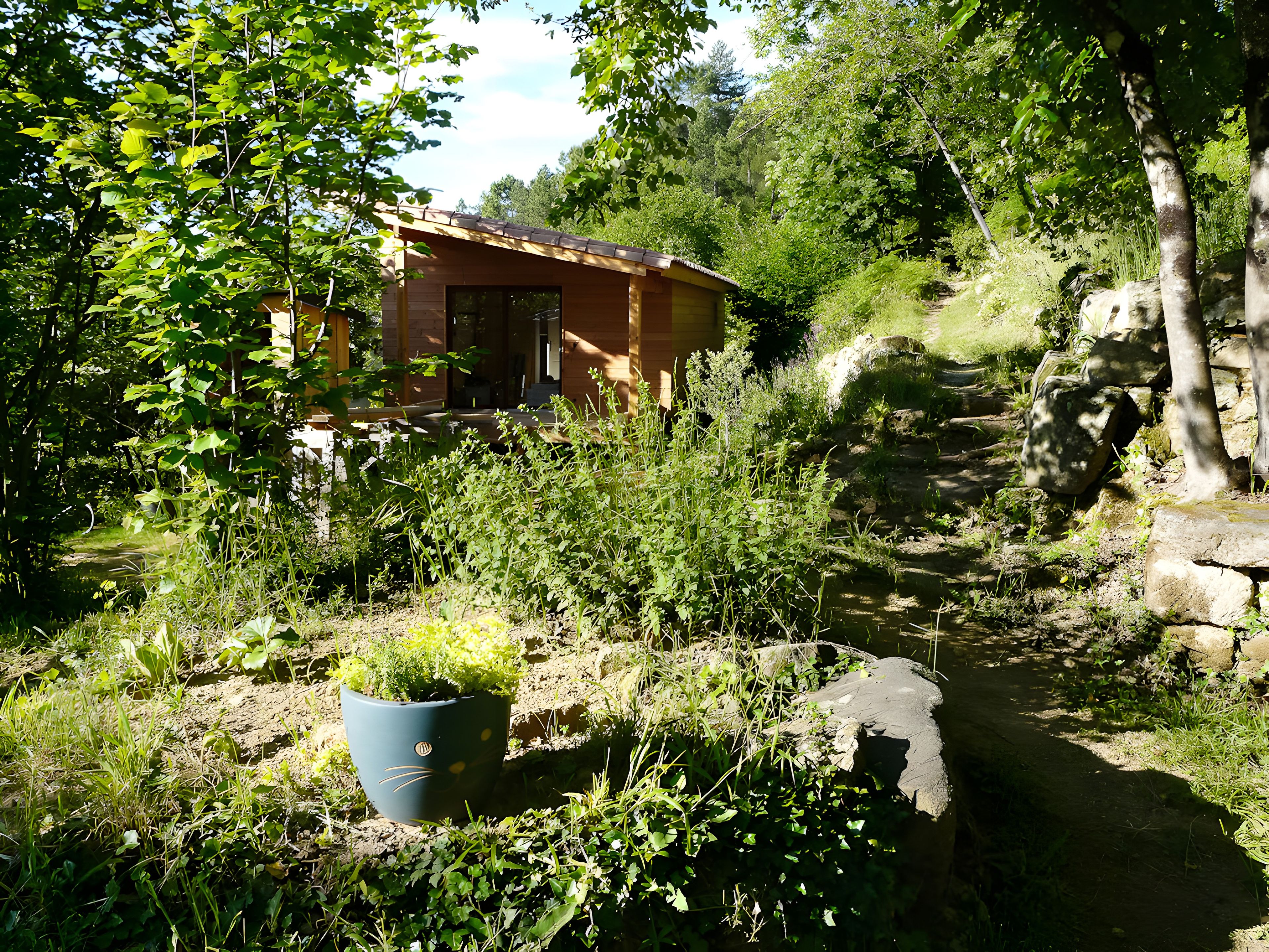 Een rustiek vakantiehuisje, omringd door weelderige begroeiing en een stenen muur.