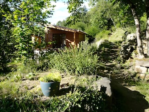 Eine rustikale Holzhütte, umgeben von dichtem Grün und einer Steinmauer.
