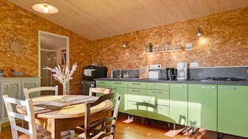 A kitchen with a wooden ceiling, green cabinets, a dining table with chairs, and a vase with flowers.