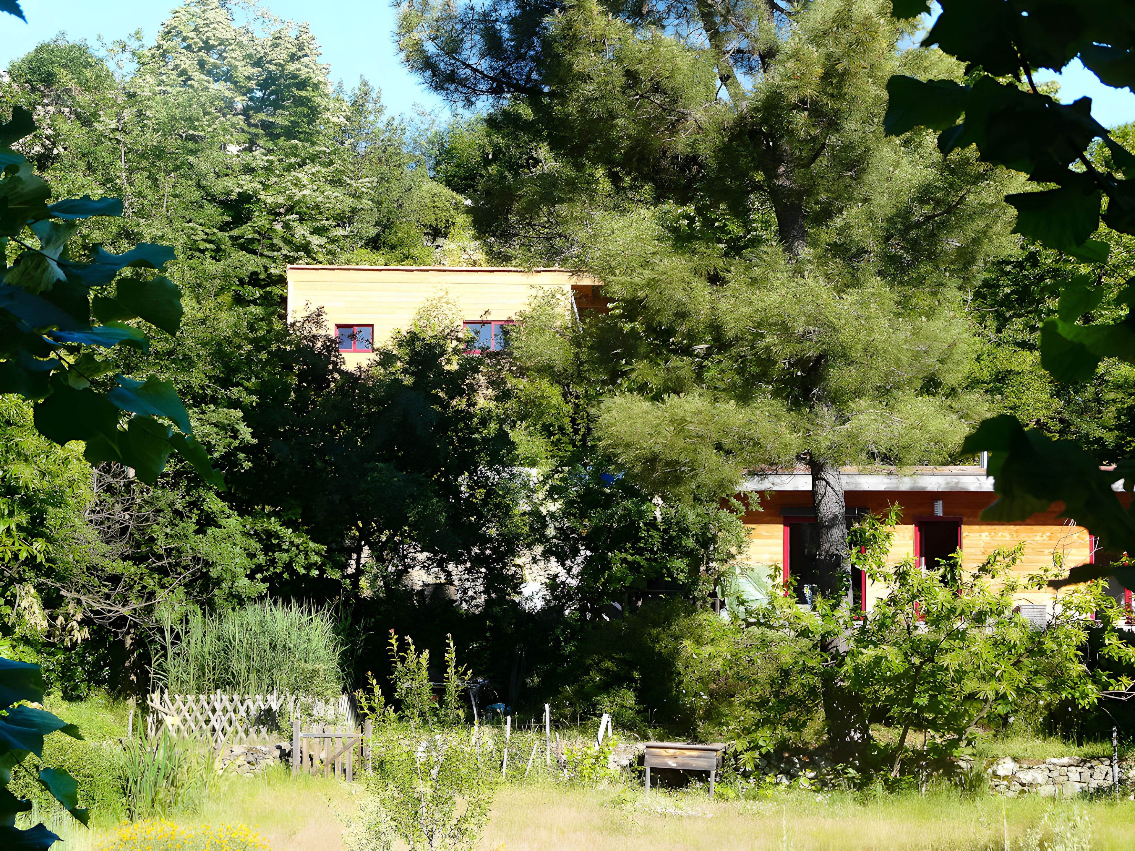 A yellow building with a red door, surrounded by trees and a white fence.