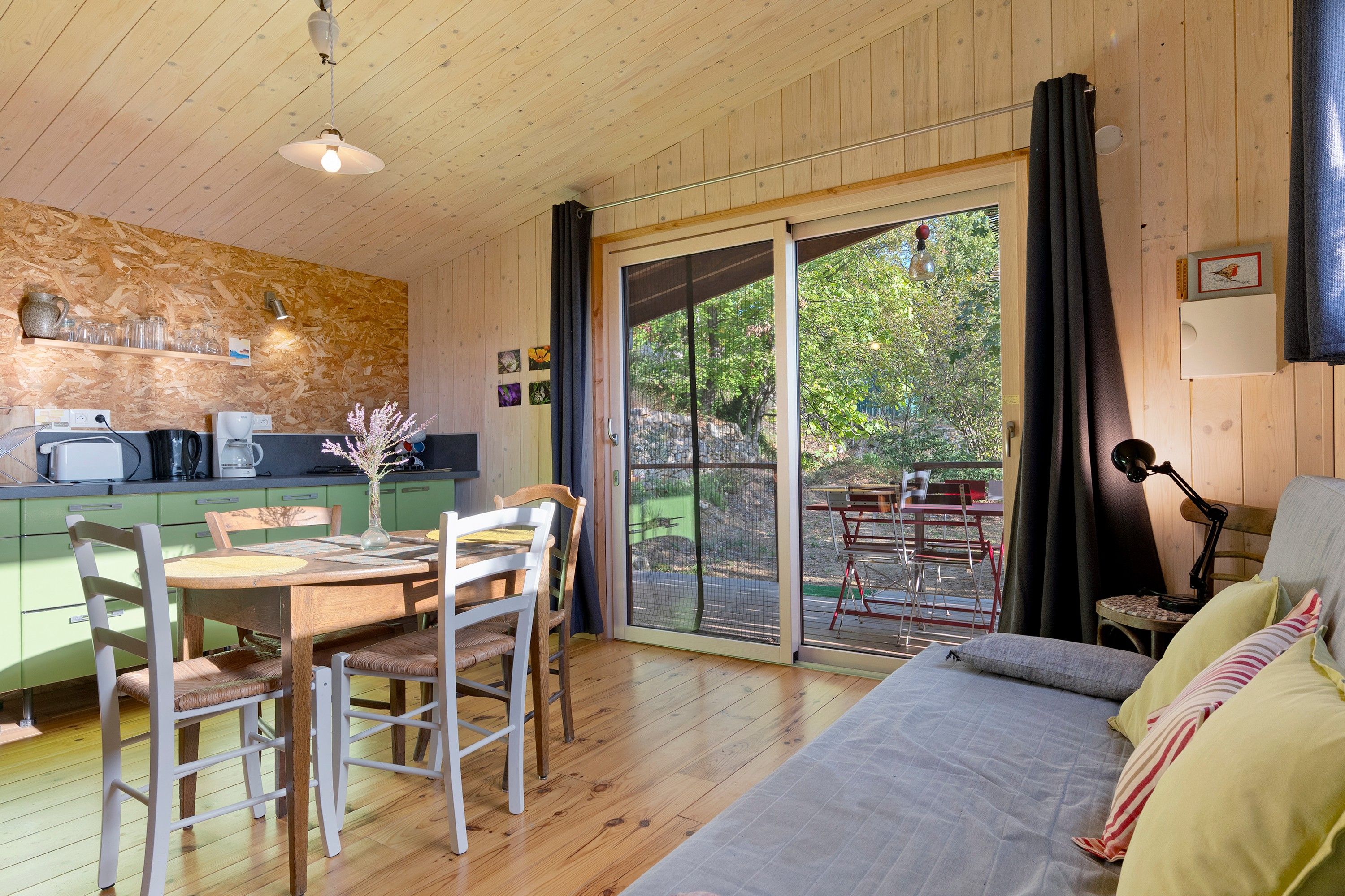 Interior acogedor de una cabaña con zona de comedor, sofá y puerta corredera de vidrio que da a un patio exterior.