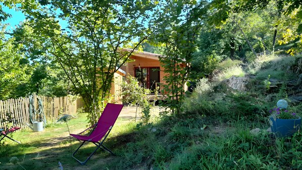 A wooden cabin with a porch, surrounded by lush greenery and a wooden fence. - Holiday Home 'Cabane De La Grande Ourse -' with Mountain View, Private Garden and Wi-Fi (Banne)