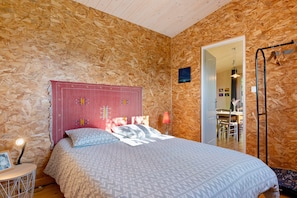 A bedroom with a wooden wall, a bed with patterned bedding, a nightstand, a lamp, and a framed picture.