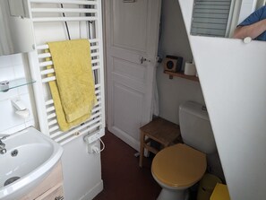 A compact bathroom with a white sink, a yellow towel, a wooden stool, and a toilet with a wooden seat. - Charming 40m² apart for 2 people – Paris 10 (Paris)