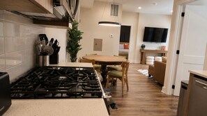A modern kitchen with a gas stove, wooden dining table, and a TV mounted on the wall. - The James Suite Three | New 2BR Beach Block (Atlantic City)