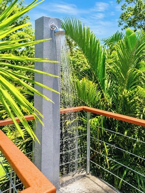 Ein Betonbrunnen mit einem Metallauslauf, umgeben von üppigem Grün und einem Metallgeländer.